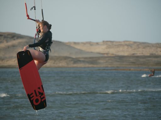 Kitesurferin springt über das Wasser und berührt dabei das Brett an der Spitze.