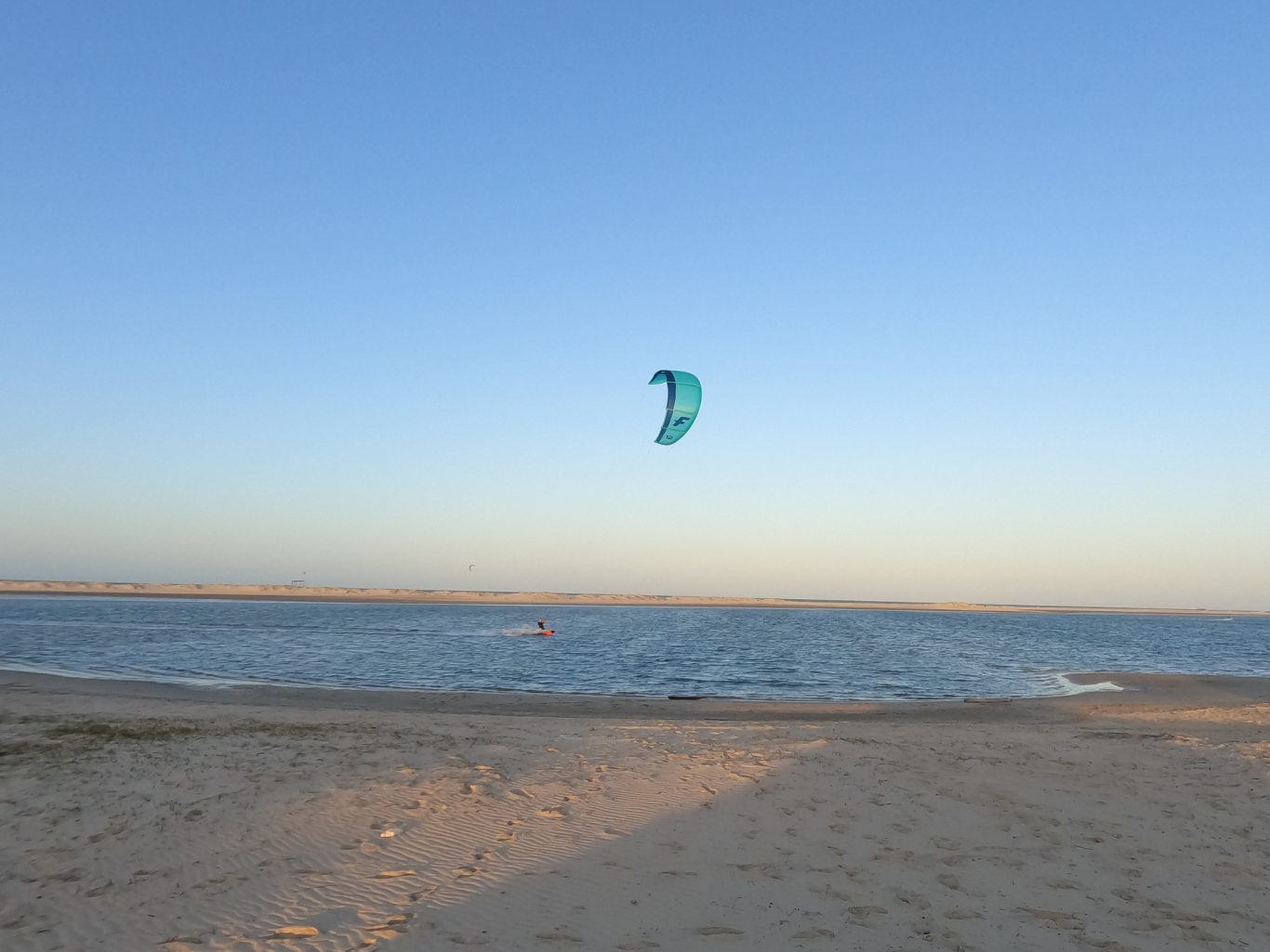 Kitesurfer mit blauem Kite über dem ruhigen Wasser bei Sonnenuntergang.