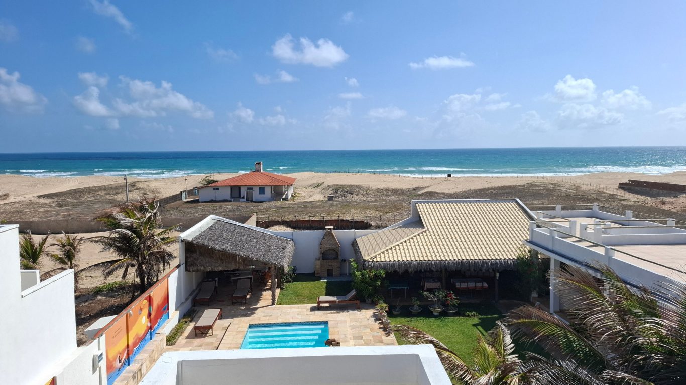 Strandblick mit buntem Haus, Pool und Sonnenschirmen in der Nähe des Wassers.