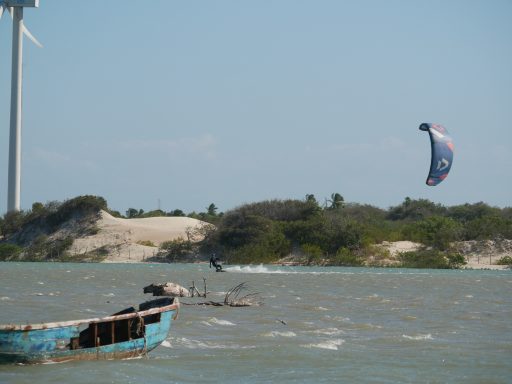 Altes Fischerboot im Vordergrund, Kitesurfer und Dünen im Hintergrund.