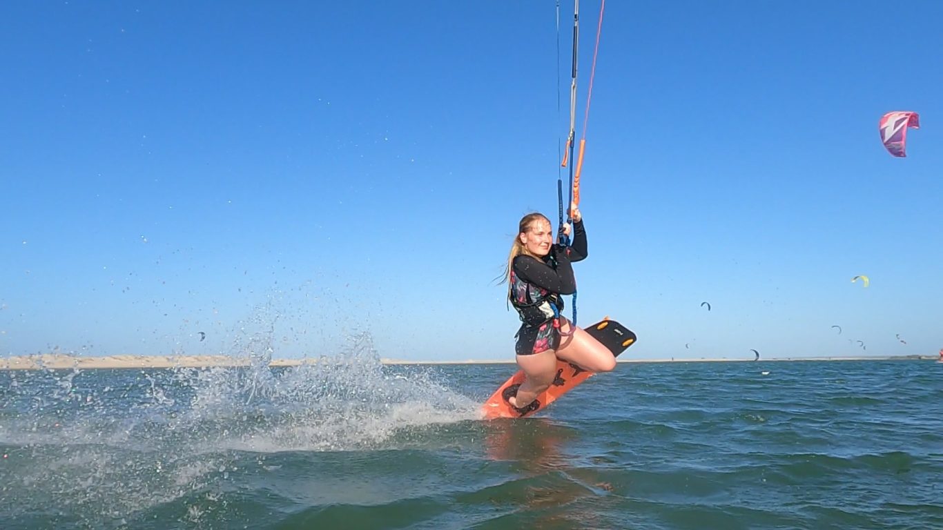 Ein Frau kitet und macht einen Darkslide übers Wasser bei Sonnenschein.