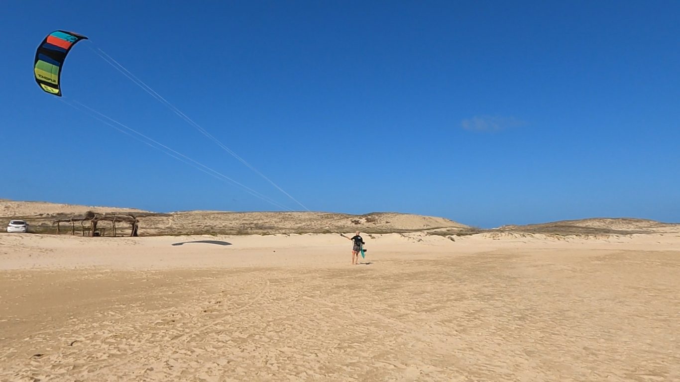 Kitesurfer an einem weiten Sandstrand unter klarem blauen Himmel.
