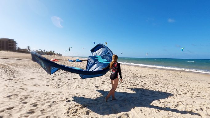 Frau am Strand mit einem Kite in der Hand, Himmel blau, Meer im Hintergrund