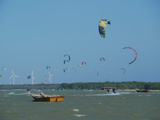 Kitesurfer in Aktion mit Booten und Windkraftanlagen im Hintergrund.