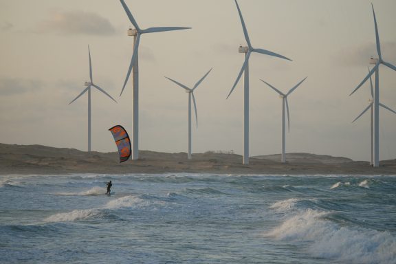 Kitesurfer im Wasser vor Windkraftanlagen und einem bewölkten Himmel.