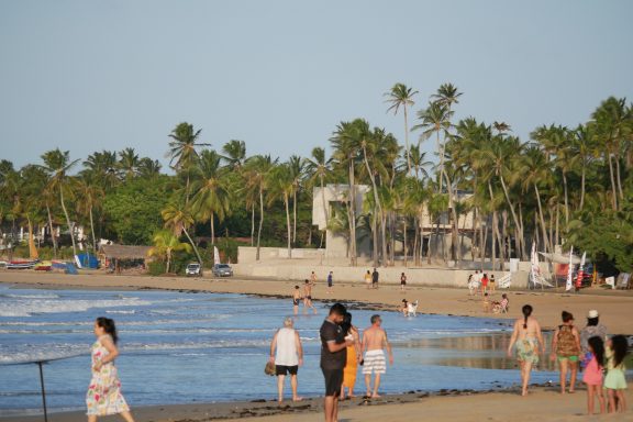 Strand mit Palmen, Menschen spazieren am Wasser entlang und entspannen.